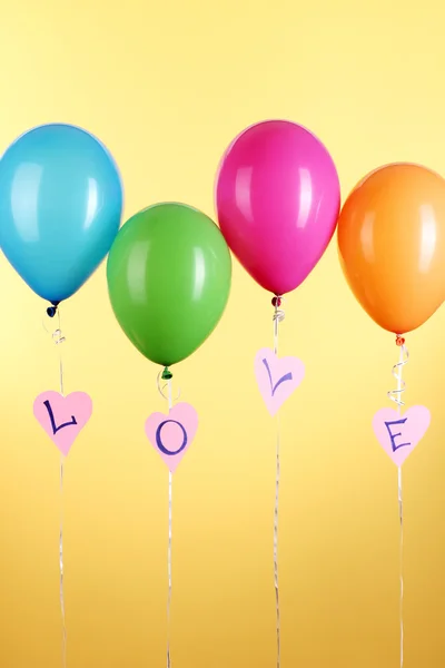 Bunte Luftballons halten Wort Liebe auf gelbem Hintergrund — Stockfoto