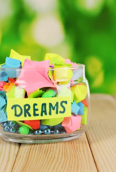 Glass vase with paper stars with dreams on wooden table on natural backgrou — Stock Photo, Image