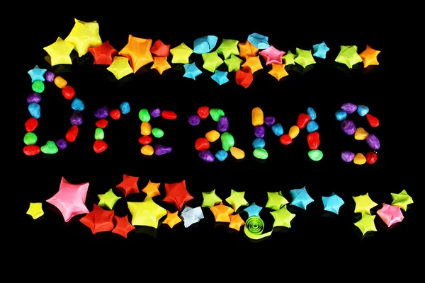 The word Dreams with colorful paper stars with dreams isolated on black — Stock Photo, Image