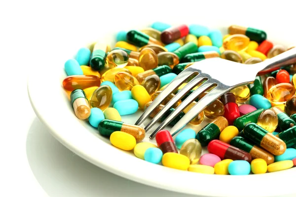 Capsule e pillole colorate su piastra con forchetta, isolate su bianco — Foto Stock