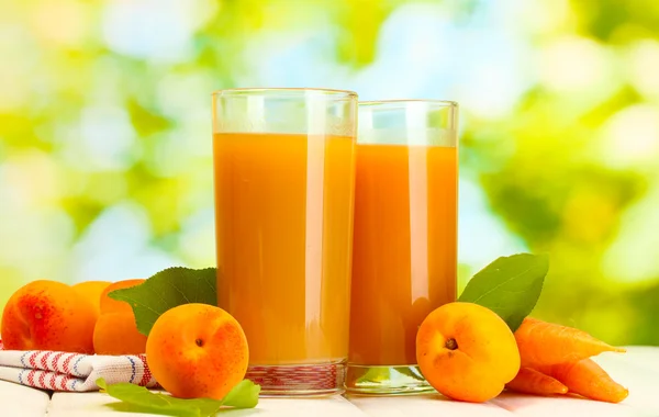 Glasögon med morot och aprikos juice på vita träbord på grön backgro — Stockfoto