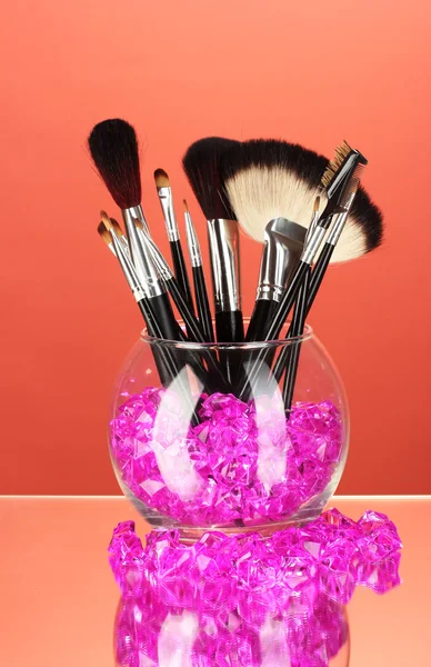 Make-up brushes in a bowl with stones on red background — Stock Photo, Image