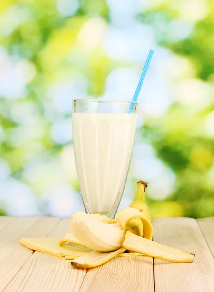 Banana milk shake on wooden table on bright background — Stock Photo, Image