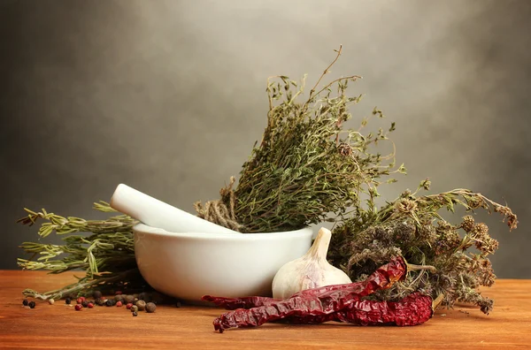 Hierbas secas en mortero y verduras, sobre mesa de madera sobre fondo gris —  Fotos de Stock