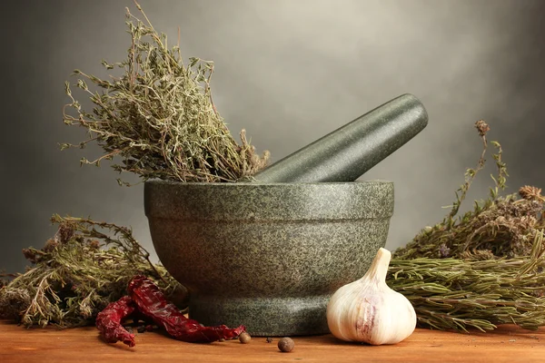 Dried herbs in mortar and vegetables, on wooden table on grey background — Stock Photo, Image