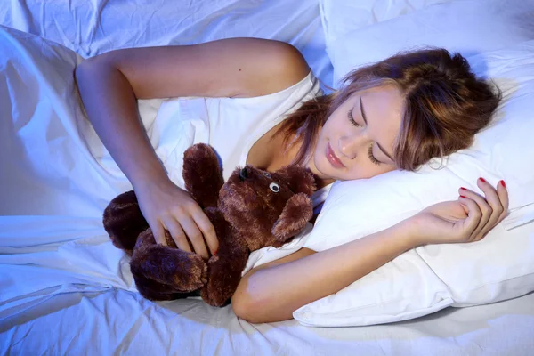 Jeune belle femme avec ours jouet dormant sur le lit dans la chambre — Photo