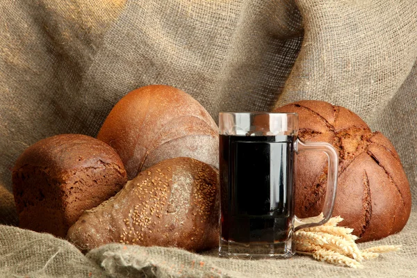 Tankard of kvass and rye breads with ears, on burlap background — Stock Photo, Image