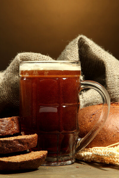 tankard of kvass and rye breads with ears, on wooden table on brown backgro