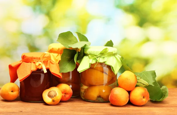 Canned apricots in a jars and sweet apricots on wooden table on green backg — Stock Photo, Image