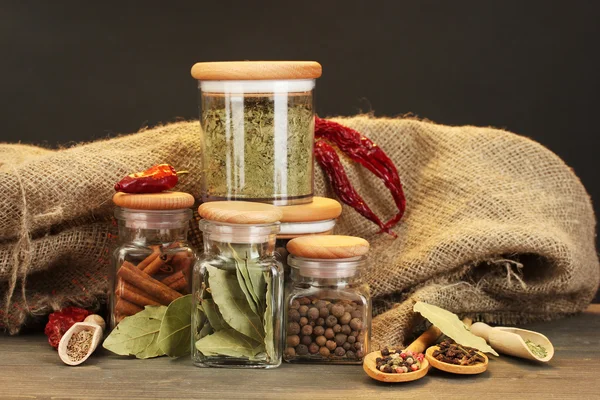 Jars and spoons with spices on wooden table on black background — Stock Photo, Image