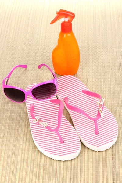 Chaussons de plage roses avec lunettes de soleil et crème solaire sur le tapis — Photo