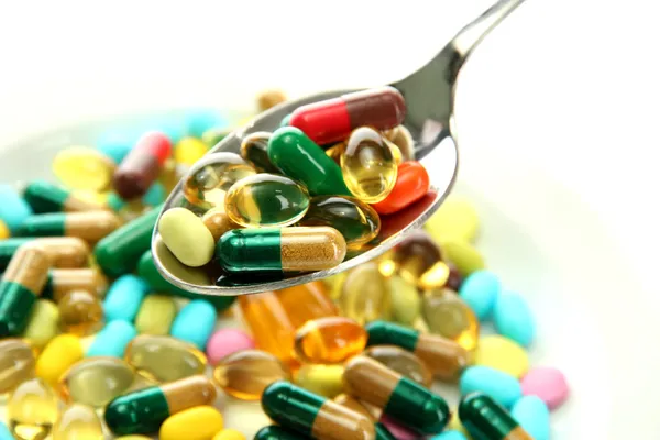 Colorful capsules and pills on plate with spoon, close up — Stock Photo, Image