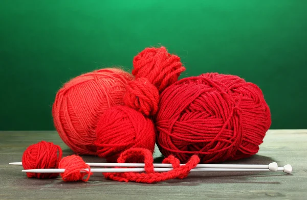 Red knittings yarns on wooden table on green background — Stock Photo, Image