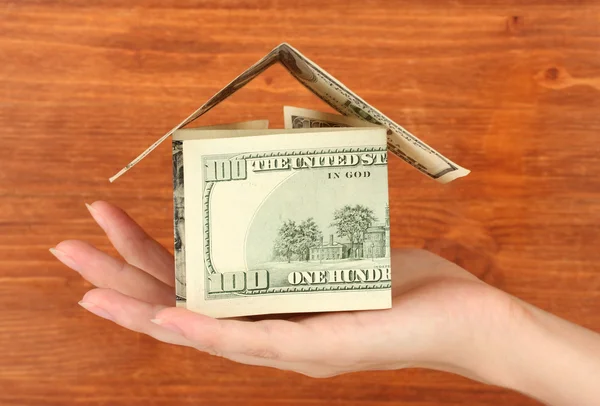 Mão segurando uma casa feita de dólares em fundo de madeira close-up — Fotografia de Stock