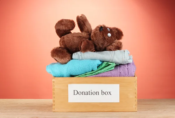 Donation box with clothing on red background close-up — Stock Photo, Image