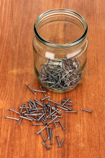 Metal nails and glass jar on wooden background — Stock Photo, Image