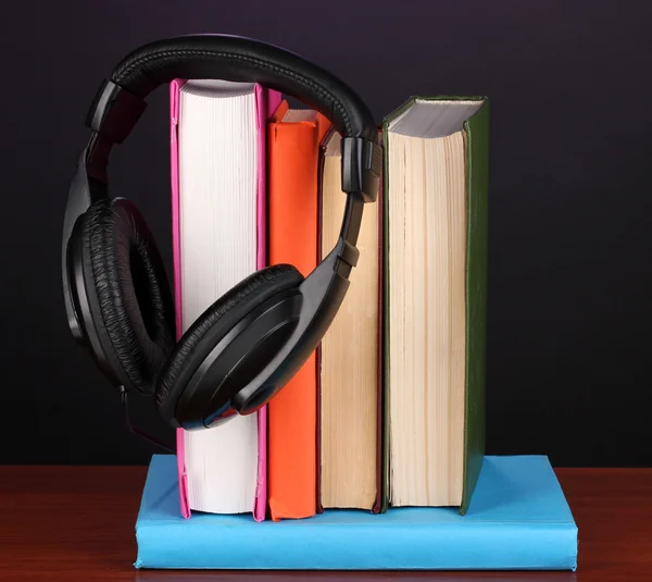 Hörlurar på böcker om träbord på svart bakgrund — Stockfoto