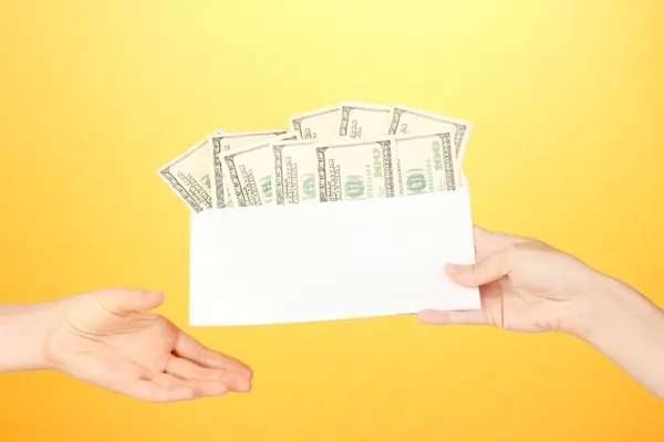 Ręka kobiety przechodzi kopertę z wynagrodzenia na żółtym tle — Zdjęcie stockowe