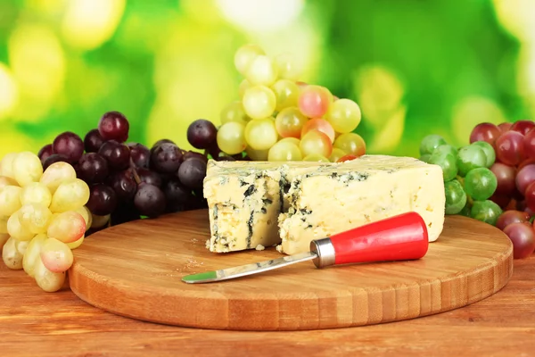 チーズ、まな板の上の明るい緑の背景のブドウと型 — ストック写真