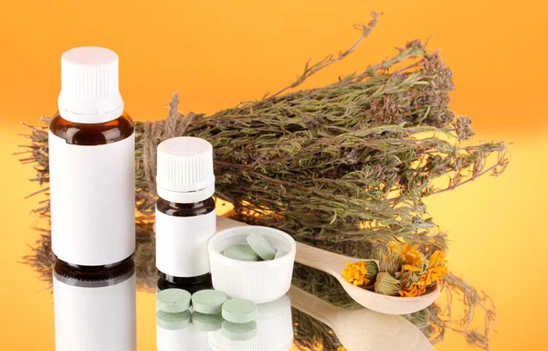 Flessen van geneesmiddelen en kruiden op oranje achtergrond. concept van de homeopathie — Stockfoto