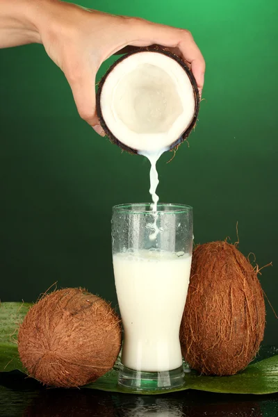Женская рука наливает кокосовое молоко в стакан на зеленом фоне — стоковое фото