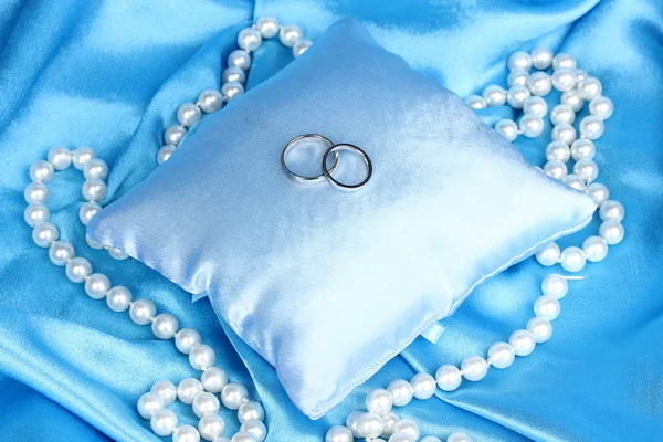 Anillos de boda en almohada de satén sobre fondo de tela azul — Foto de Stock