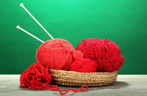 Red knittings yarns in basket on wooden table on green background — Stock Photo, Image