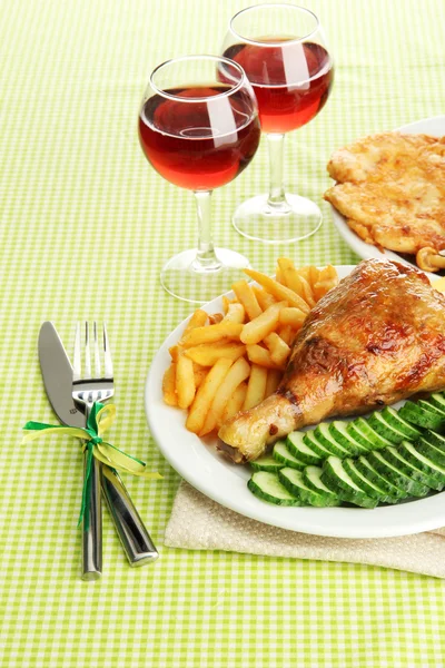 Roast chicken with french fries and cucumbers, glasses of wine on green tab — Stock Photo, Image