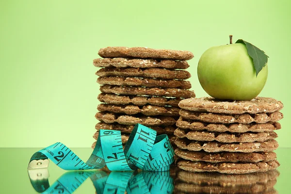 Tasty crispbread, apple and measuring tape, on green background — Stock Photo, Image