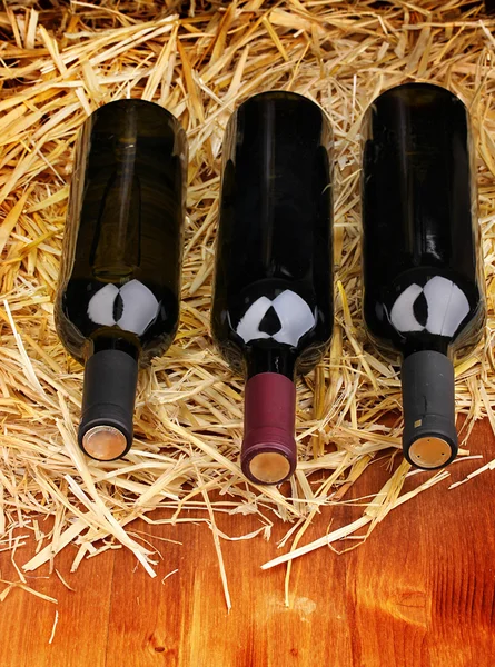 Бутылки отличного вина на сене на деревянном столе — стоковое фото