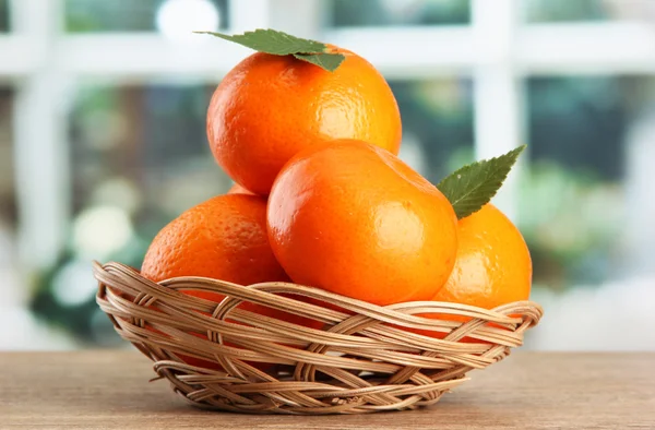 Tangerines with leaves in a beautiful basket, on wooden table on window bac — Stock Photo, Image