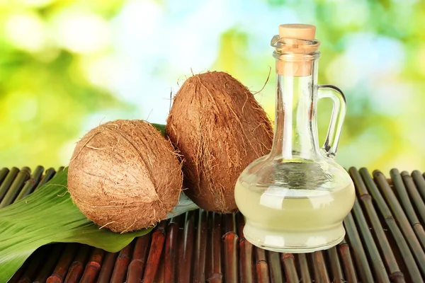 Dekanter mit Kokosöl und Kokosnüssen auf grünem Hintergrund — Stockfoto
