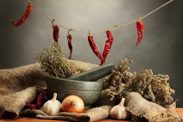 dried herbs in mortar and vegetables, on wooden table on grey background