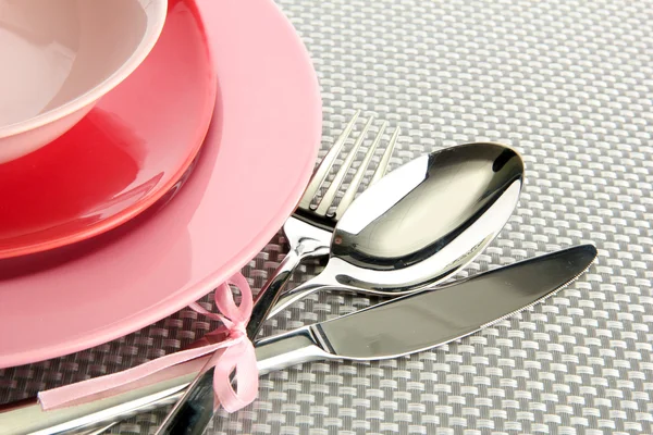 Assiettes vides roses avec fourchette, cuillère et couteau sur une nappe grise — Photo
