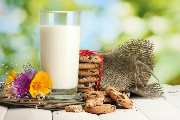 Glass of milk, chocolate chips cookies with red ribbon and wildflowers on w — Stock Photo, Image