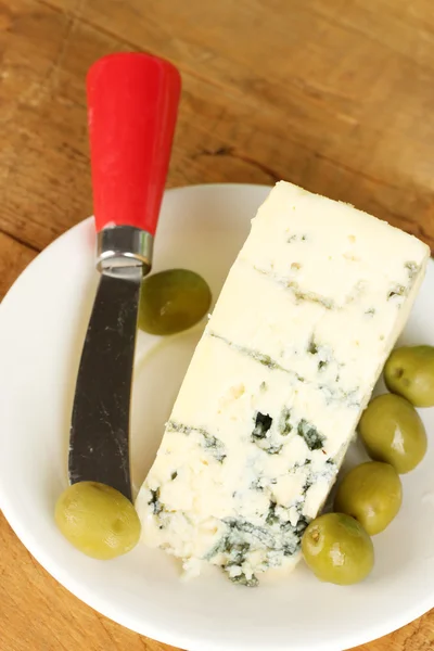 Cheese with mold and olives on the plate and knife on wooden background clo — Stock Photo, Image