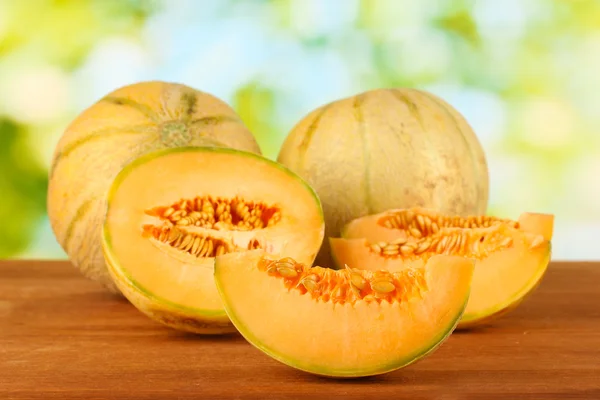 Geschnittene Melone auf Holztisch auf grünem Hintergrund — Stockfoto