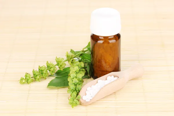 Flacone di medicinale con compresse e fiori su tappetino di bambù — Foto Stock