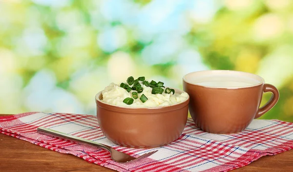 Kartoffelpüree in Schüssel und Tasse mit Milch auf bunter Serviette auf Holzplatte — Stockfoto