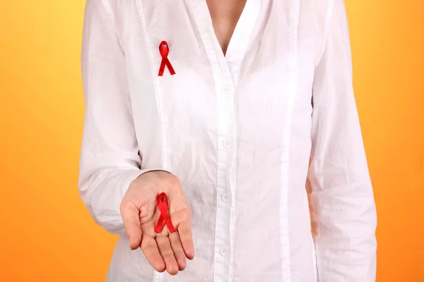 Woman with red ribbon in hands on orange background — Stock Photo, Image