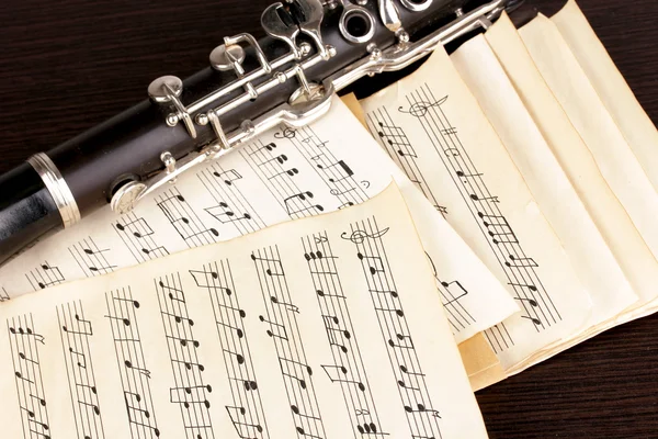 Musical notes and clarinet on wooden table — Stock Photo, Image