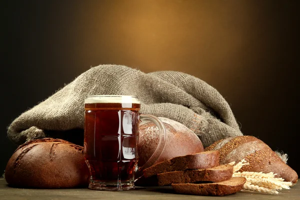 Tankard de kvass y panes de centeno con orejas, sobre mesa de madera sobre fondo marrón —  Fotos de Stock