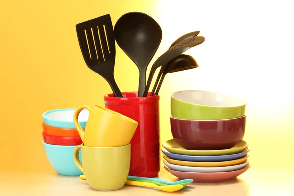 Bright empty bowls, cups and kitchen utensils on wooden table on yellow bac — Stock Photo, Image