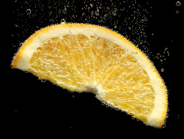 Fatia de laranja na água com bolhas, no fundo preto — Fotografia de Stock