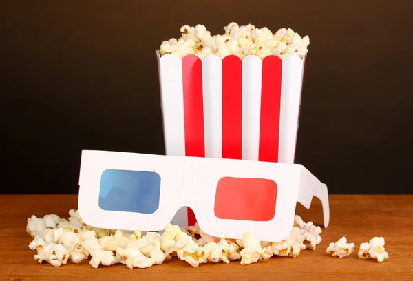 Popcorn and cinema glasses on wooden table on brown background — Stock Photo, Image