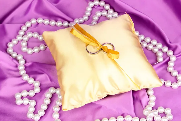 Anneaux de mariage sur oreiller en satin sur fond de tissu violet — Photo