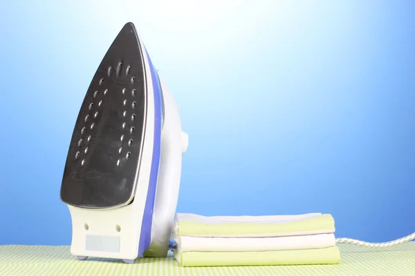 Bügeleisen und Handtücher auf grünem Stoff auf blauem Hintergrund — Stockfoto