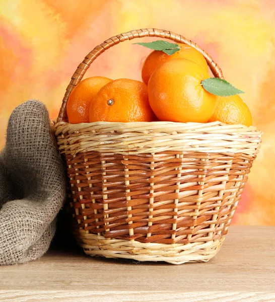 Tangerines with leaves in a beautiful basket, on wooden table on orange bac — Stock Photo, Image