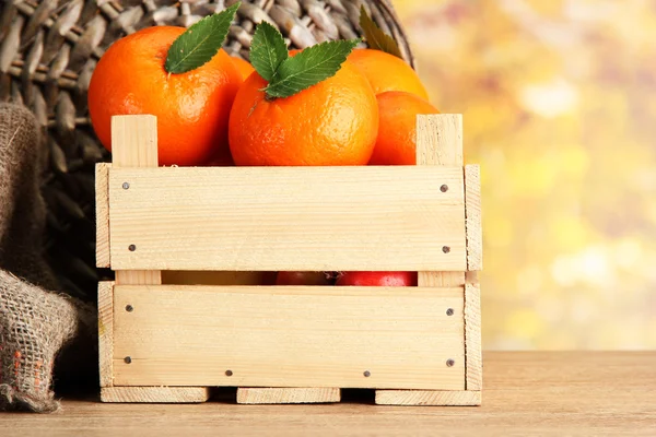 Tangerinas saborosas maduras com folhas em caixa de madeira na mesa em backgrou laranja — Fotografia de Stock