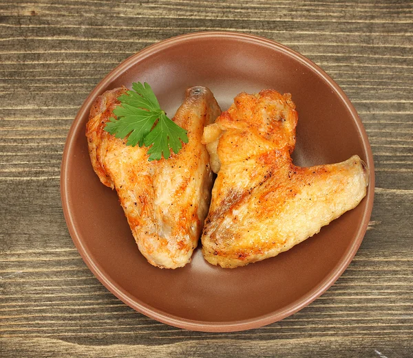 Roasted chicken wings with parsley in the plate on wooden background close- — Stock Photo, Image